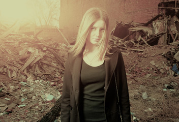 Young blond haired girl posing alone in slums backlit, toned col
