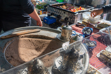Obraz premium Preparing and cooking Turkish coffee with sand and a cezve. Turkish style coffee in its equipment in temporary booth outdoor cafe at outdoor market in Europe. 