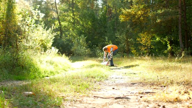 male volunteer cleaner in the signal orange vest cleans garbage in the forest, cleansing the forest and nature from garbage, garbage and nature, rubbish