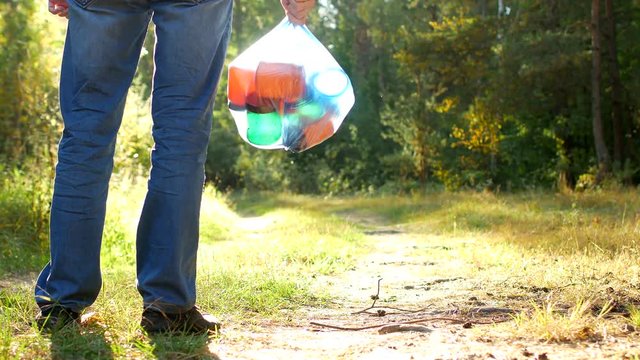A man in a forest clearing stands with a package of garbage in his hands, a garbage collector, garbage and nature, close-up