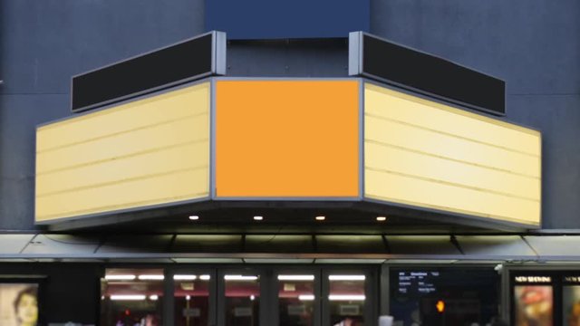 A daytime view of a theater's blank marquee in a large city as pedestrians and traffic pass by.  	