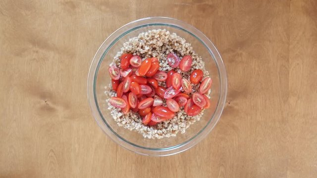 Adding vegetables to bowl of farro, close up