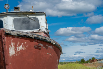 An abandoned and weathered red rusty boat sits in a marshy grass field along the Homer Spit, along the Kachemak Bay in Homer Alaska