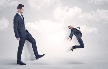 Big businessmen kicking himself as a small employee with cloudy background
