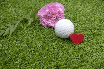 Golf ball with pink carnation and red heart on green 