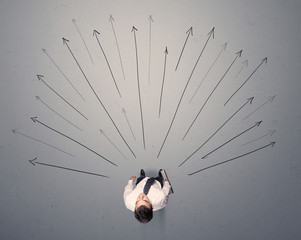 Young contemplating businessman stands in front of grey arrows 