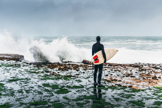 Surfer looking at the waves crushing on the cliff