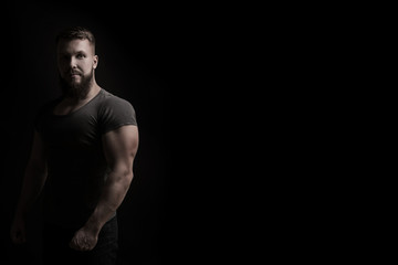 Bodybuilder portrait. Muscular man in a tight t-shirt. Dramatic portrait in unsaturated colors. - obrazy, fototapety, plakaty