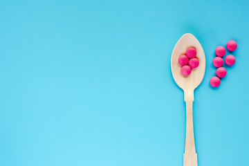 Wooden spoon with pink ibuprofen pills on blue background for healthcare and medical concept