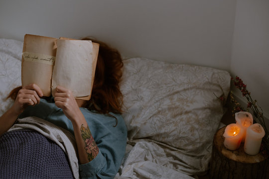 woman reading on bed close to candles