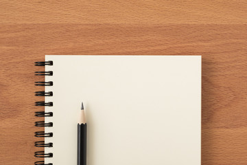 Top view of open spiral blank notebook with pencil on wood desk background