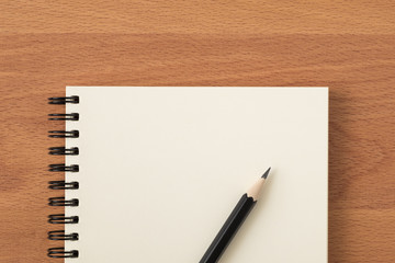 Top view of open spiral blank notebook with pencil on wood desk background