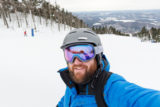 Bearded man pauses to take a selfie while skiing down a mountain