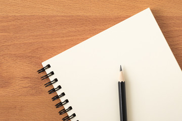 Top view of open spiral blank notebook with pencil on wood desk background