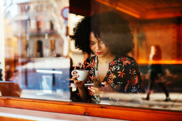 Afro woman using phone taking a coffee in a restaurant.