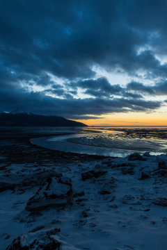 Winding curved river flowing and jetting out to seashore with gloomy clouds and sunset in distance