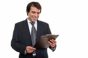 Studio shot of young happy Persian businessman smiling while rea