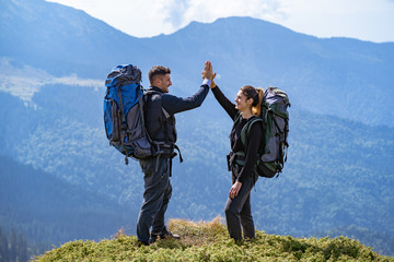 The happy couple with backpacks standing on the mountain landscape background