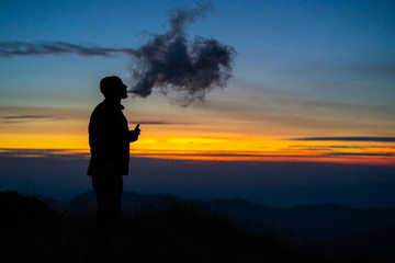 The man smoking an electronic cigarette on the sunset background