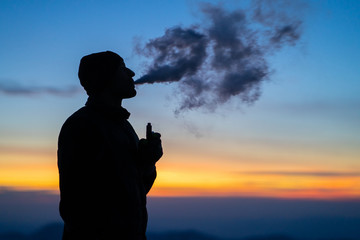 The man smoking an electronic cigarette on the sunset background
