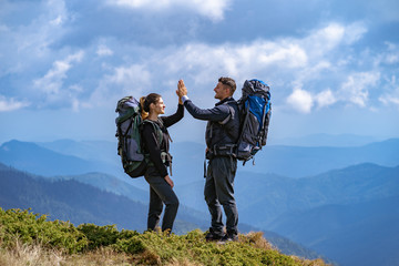 The happy couple with backpacks gesturing on the mountain