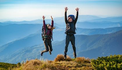 The man and a woman with backpacks jumping on the mountain