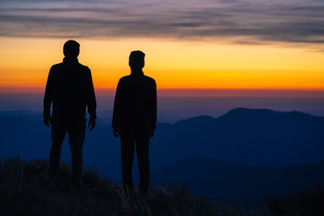 The couple standing on the mountain on a sunrise background