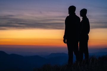 The silhouette of the couple on the mountain with a sunrise background