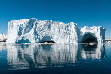Fototapeta na wymiar Large weathered iceberg with caves reflected in glassy water, Cierva Cove, Antarctic Peninsula