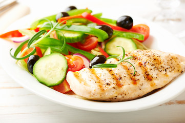Grilled chicken breast with green and red pepper, cherry tomatoes, lettuce, black olives, cucumber, pink pepper and fresh rosemary. Home made food. Concept for a tasty and healthy meal. Close up.