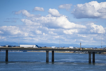 Fototapeta premium Long bridge across the Columbia River with heavy traffic of semi trucks and another cars on the background of cloudy sky