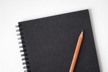 Top view of notebook black cover with wood texture pencil on white desk background