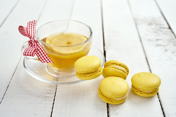 delicious and sweet macaroons and hot tea with lemon on an old white wooden table