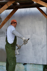 Worker in overalls and cap painting primer on wall with roller before plastering. Facade thermal...