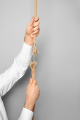 Man climbing frayed rope on gray background