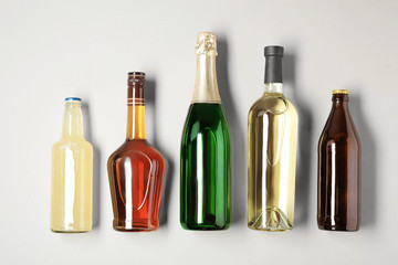 Bottles with different alcoholic drinks on light background, top view