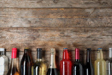 Bottles with different alcoholic drinks on wooden background, top view. Space for text