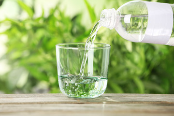 Pouring water from bottle into glass on table against blurred background
