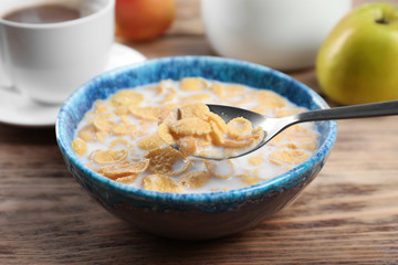 Healthy cornflakes with milk in bowl served on wooden table, closeup