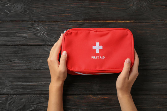 Woman Holding First Aid Kit On Dark Table, Top View