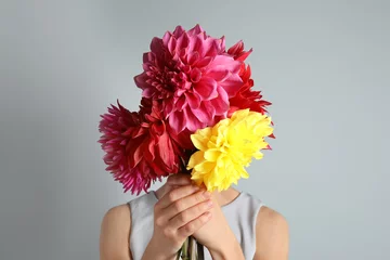 Fototapeten Woman holding bouquet of beautiful dahlia flowers against gray background © New Africa