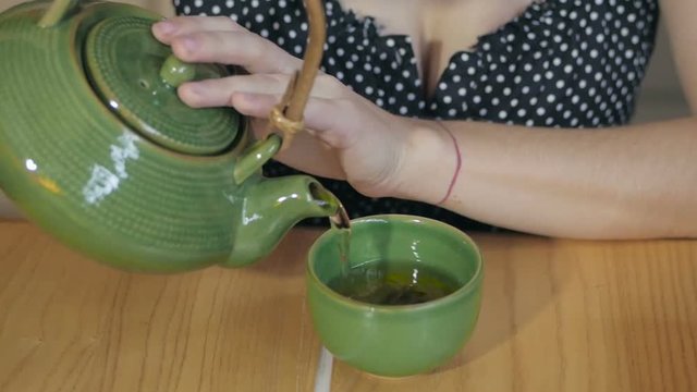 Young woman pours tea from a teapot into a green cup