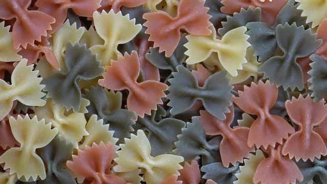 Multicolored pasta background, rotating, top view. Rotation of colored farfalle pasta. Heap of uncooked pasta. Italian food close up. Delicious italian farfalle tricolor pasta, food background
