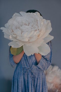 Unrecognizable woman hiding her face with giant white paper peony