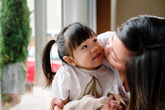 Asian Mother Kissing Her Daughter at Home