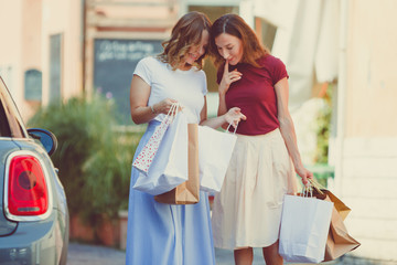 Best girlfriends showing purchases in shopper bags to each other and looking curiously. Women...