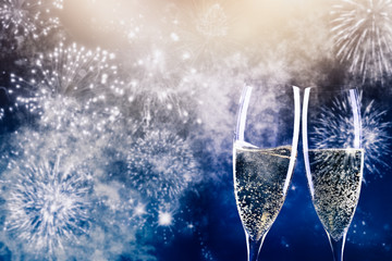 two champagne glasses ready to bring in the New Year - holiday lights and fireworks in the background