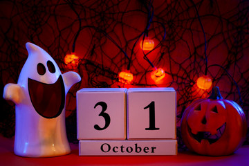 Dark halloween and fall holiday concept a calendar showing october 31 with a ghost and jack o lantern to each side and pumpkin lights hanging from a black spider web in the background at night
