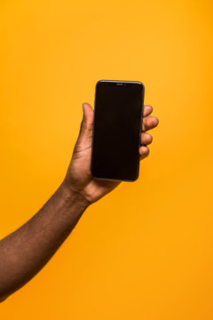 Hand holding a modern smartphone against a yellow background
