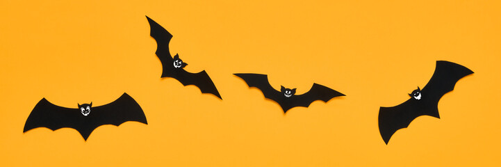 Halloween and decoration concept. Black paper bats with smiley faces flying over orange background. Halloween banner.